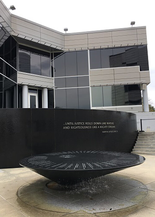 Black marble civil right monument with various events etched on it, museum in background.  Grey overcast sky.