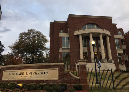 Tuskagee University main building, which is a two-story brick building with greek columns in front.  Grey cloudy sky above.