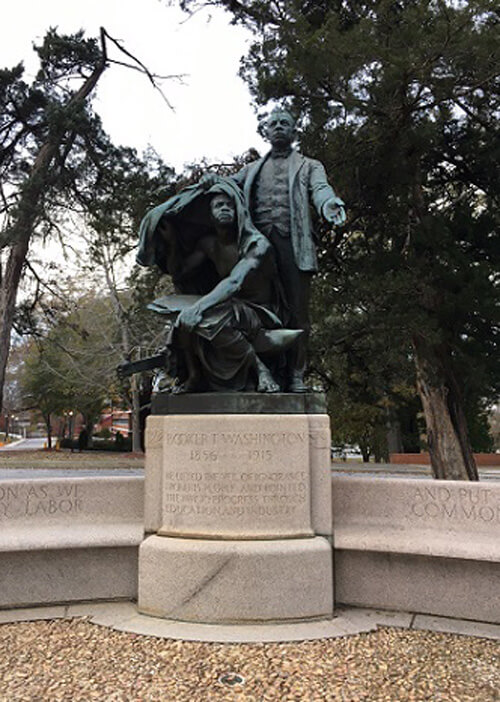 Statue of Booker T. Washington on cement stand flanked by a bench.  Overcast sky.