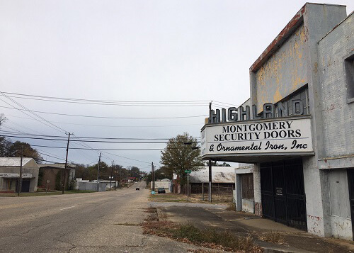 Abandoned theatre at right that says "Highland" above the marquee. Plain cement building.  Grey sky above.