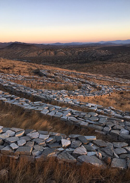 Series of ordered stones in ground, spelling out some ancient symbols called the "Rhythm of Life" at sunrise.