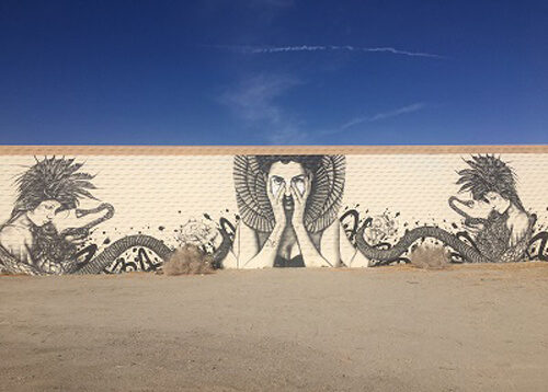 Mural of a lady with serpents for hair on side of building, blue sky with no clouds.