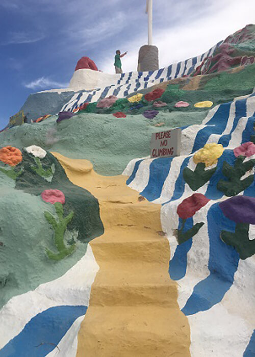 Brightly painted hill with yellow painted stairway in between blue and white stripes, painted flowers and painted green patches, part of the Salvation Mountain art monument.