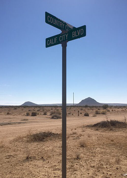 Street sign in middle of desert saying "California City Boulevard."  A couple desert hills in background, blue sky with no clouds.