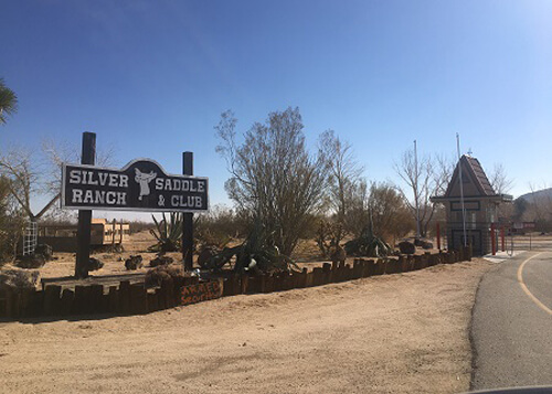 Sign at left saying "Silver Ranch Saddle and Club," entry security check in window at right.  Blue sky with no clouds.