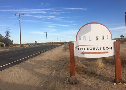 UFO shaped sign at right saying "Integratron" with arrow pointing left.  Blue sky with a few scattered clouds.