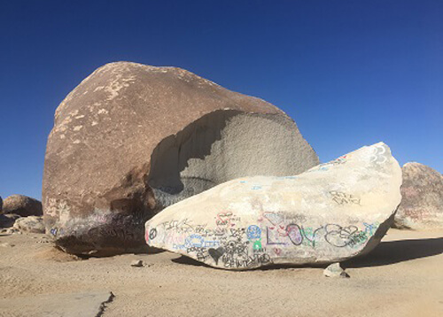 Massive boulder at left and a slice of the rock that fell off laying at right.  Blue sky with no clouds.