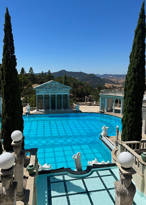 Overlooking large pool, with greek columns and statues at Hearst Castle. Blue sky above.