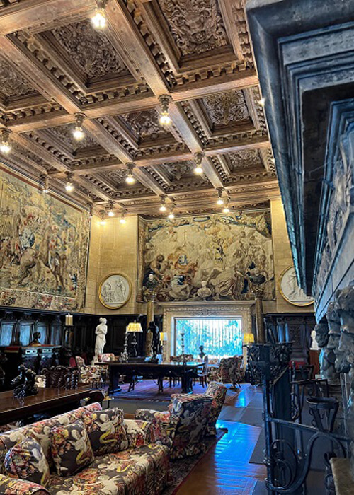 Massive living room at Hearst Castle, with many couches, eight-foot high fireplace and tapestries hanging from walls.