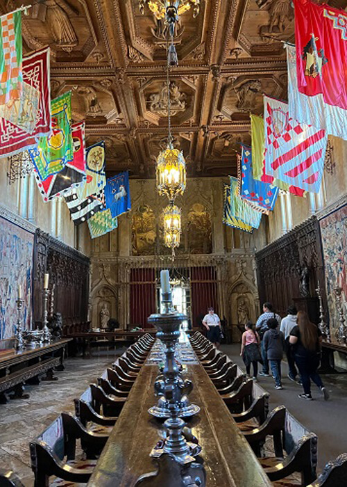 Dining table that could seat over 20 people, with various flags above and ornate ceiling designs at the Hearst Castle.