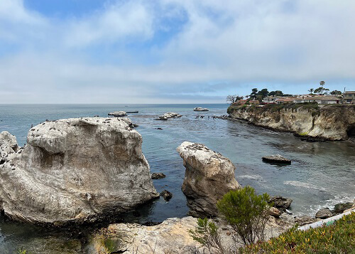 Looking down at series of rock islands on the edge of the ocean from vista point a vista point. Blue sky with some clouds above.