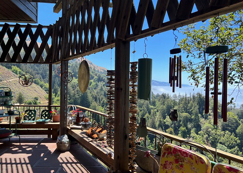 Overlooking trees from a covered wooden deck with various wind chimes and ornaments. Blue sky in the background. 