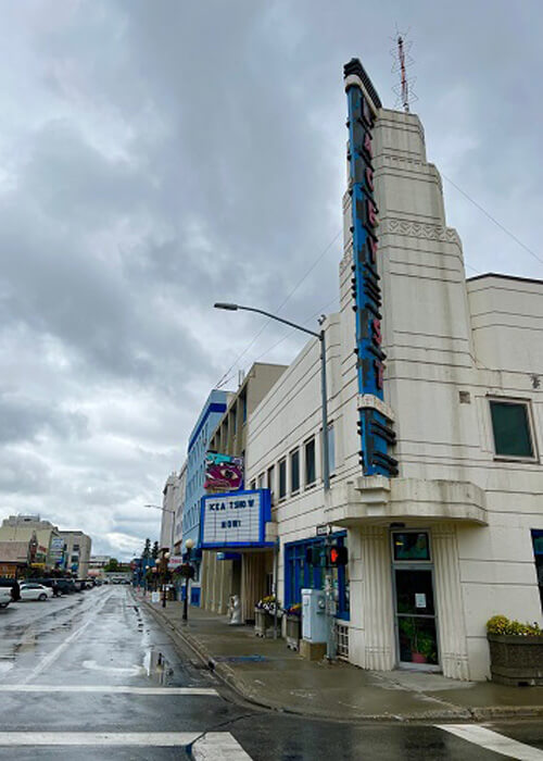 Art Deco theatre that says "Lacey" with downtown Fairbanks in background, cloudy sky above