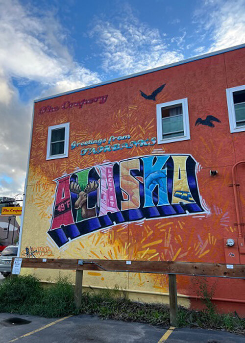 Colorful outdoor mural that says "Alaska" on an orange painted wall in downtown Fairbanks