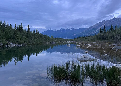 Looking down glassy river at sunrise with mountains and clouds in background