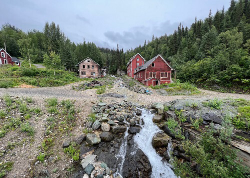 Looking up at two mining houses with stream running in between, hills in background, grey sky above