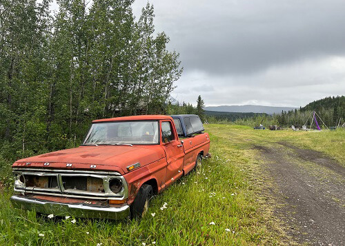 Old Orange pickup truck at left, green grassy field at right under cloudy sky