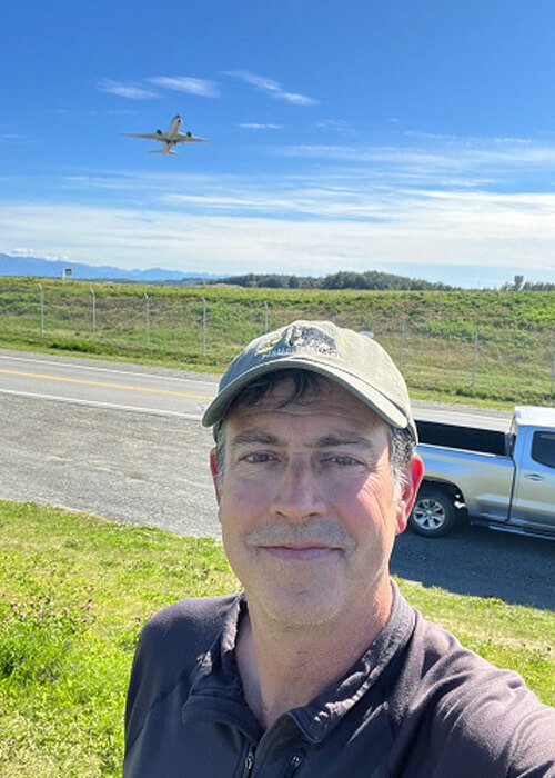 Close up of Mark Loftin with Anchorage International Airport in the background, blue sky above