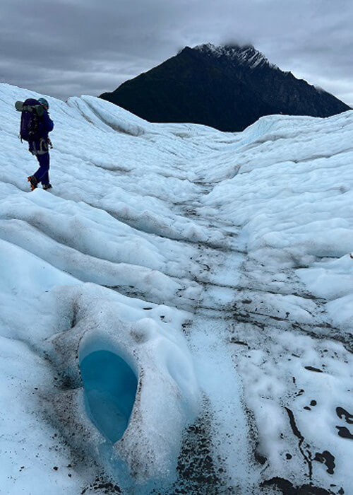 Hiker walking on blue-green glacier, grey sky above