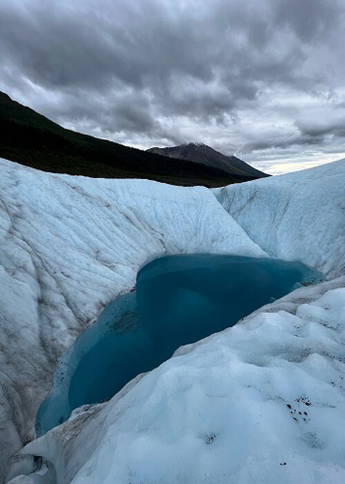 Blue pool of water in a glacier, mountains in background