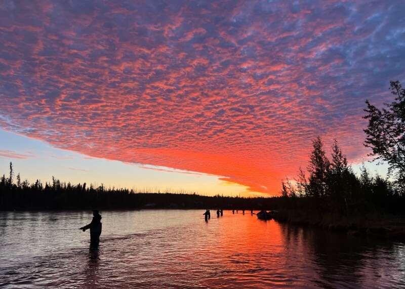 Fisherman in a river at sunrise, thick orange clouds above