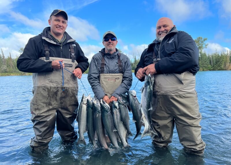 Three fishermen in the river holding a rack of sockeye salmon