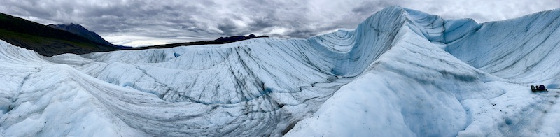 Panorama photo of glacier, with various curves and formations, cloudy sky above