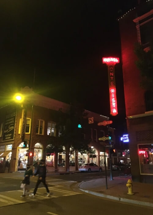 Night photo with red and yellow lights in middle, and a couple crossing the street in at bottom. Black night sky in background.