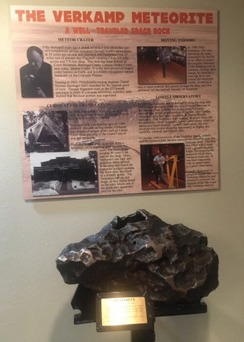 Football sized dark grey meteor rock at bottom, with wall display behind describing the Verkamp Meteorite inside a museum.