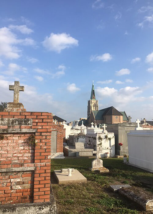 An above ground cemetery with various tomb designs, blue sky above with scattered clouds.