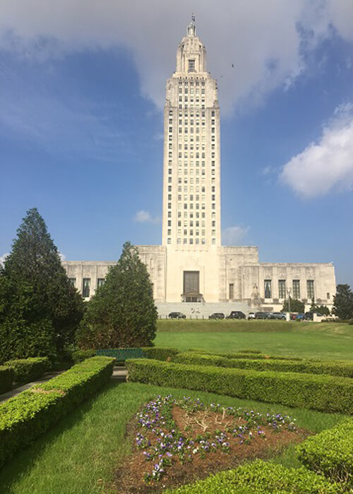 Louisiana Capitol building, tall white building with well groomed shrubs and grass in front.