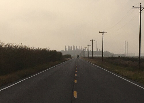 Road leading to refinery steeples in the distance, orange haze sky above. 