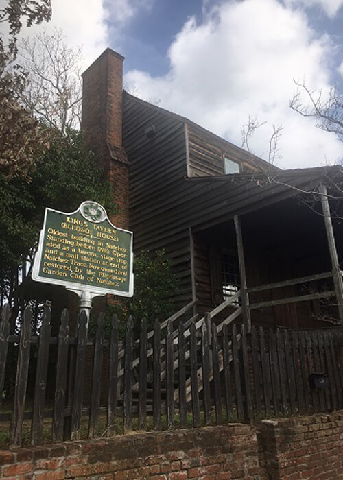 Brown wooden house built in 1769 with chimney on side. Sign in front describing its history.