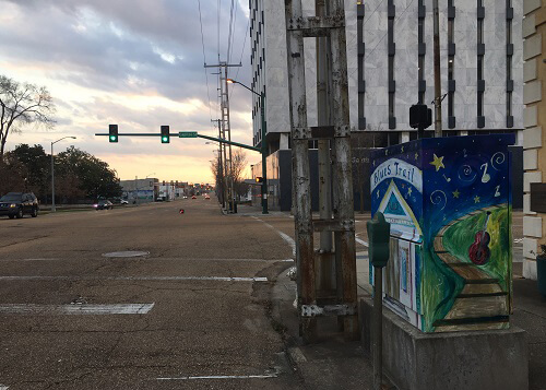 Downtown Jackson Mississippi at sunset, with painted electrical box on sidewalk at right reading "blues trail." 