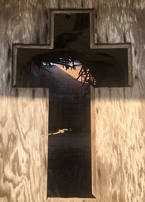 Shape of cross cut out of plywood door section at abandoned church.