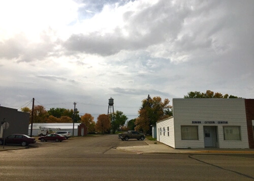 One story shop at right, and road at left leading to water tower in distance.  Cloudy skies above.