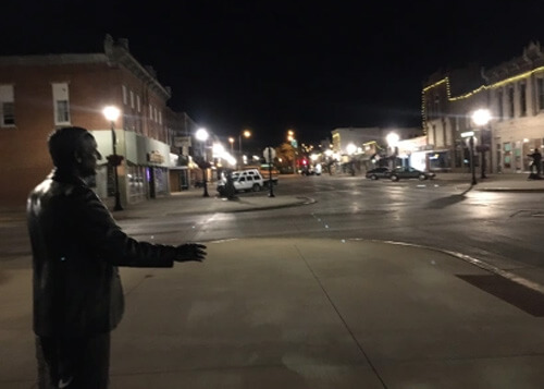 Night photo with statue at left of politician extending his hand, street light in the background.