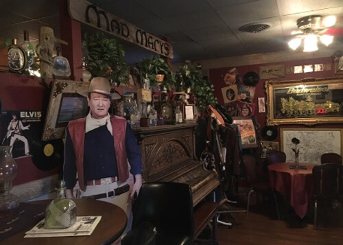 Inside Mad Mary's restaurant lobby with cardboard life-sized figure of John Wayne and old western piano behind him.