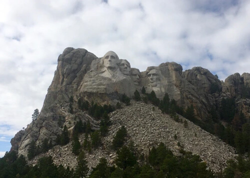 President Washington, Jefferson, Roosevelt and Lincoln's heads carved from rock at Mount Rushmore.  Cloudy sky above.