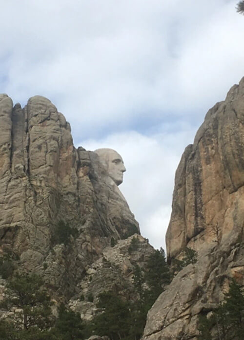 Sideview of Washington's head carved out of rock, perched on a rock cliff as part of Mount Rushmore.