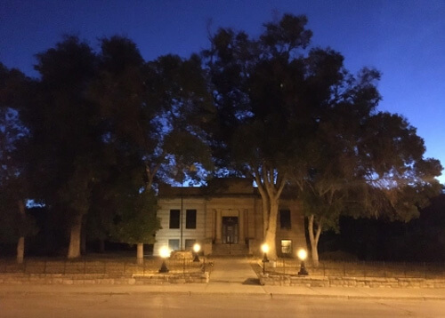 Sunrise photo of old 1920's style library surrounded by trees, dark blue sky above.