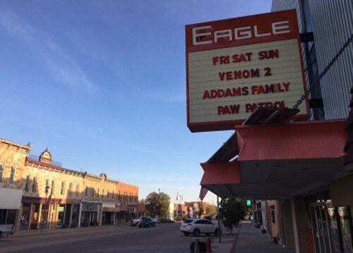 Series of old looking 1950's style buildings on both sides of street, with sign above saying "Eagle", which is a theatre.