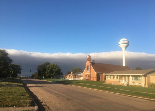 Thick layer of clouds about to cover a church and a water tower.