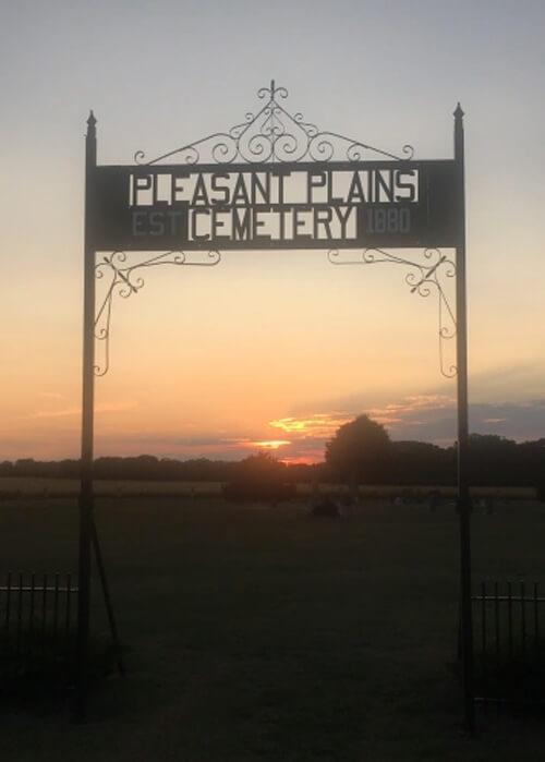 Cemetery sign above gate entry at sundown reading "Pleasant Plains Cemetery."