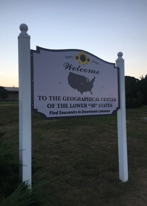 Sign reading "welcome to the geographical center of the lower 48 states" near Lebanon, Kansas.  Sundown sky behind sign.