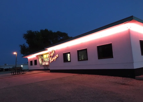 Night photo with thick streak of pink neon wrapped underneath restaurant roof, neon sign on restaurant reading "Jiffy Burger."