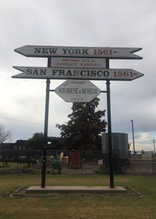 Sign showing San Francisco to the right 1561 miles and New York to the left 1561 miles.  Grey cloudy sky behind sign.