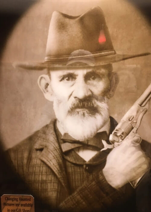 Black and white portrait picture of a random old west character with hat and holding gun.