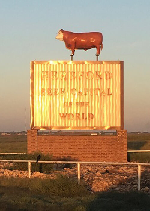 Sign with a cow on top that says "Hereford, the beef capital of the world."  Blue sky in background.