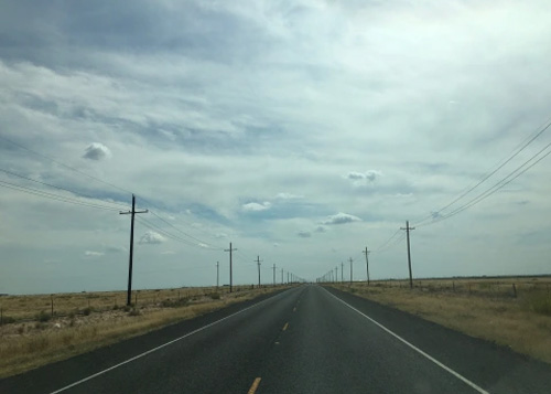 Desolate road leading into the horizon lined with telephone poles on both sides, grey cloudy sky above.